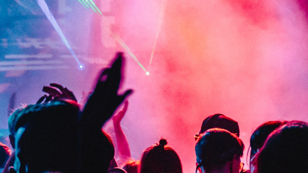 A crowd with hands raised enjoys a concert with vibrant laser lights