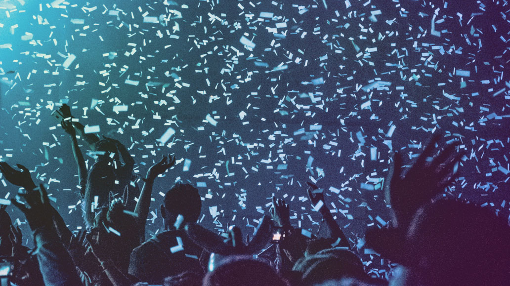 crowd of people at a concert or party are cheering with their hands in the air as confetti falls from the ceiling